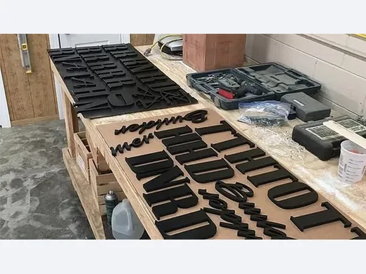 Black dimensional letters and logo components organized on a shop production bench