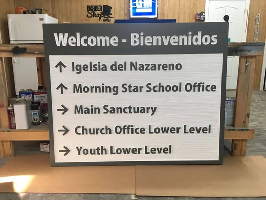 Church campus directional and wayfinding sign with bilingual welcome heading and raised arrows