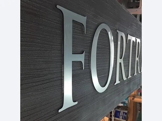 Silver dimensional letters mounted on a dark woodgrain sign panel