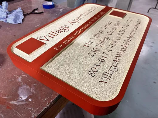 Village Apartments red and cream dimensional property information sign with textured background